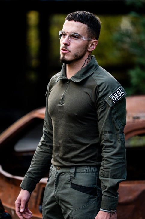Joueur airsoft en tenue tactique olive avec patch ORGA sur terrain airsoft